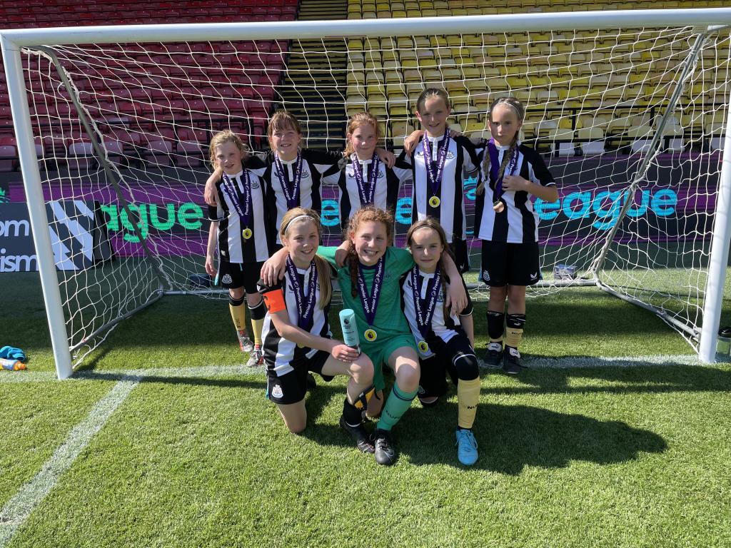 The winning team pictured in the goal, holding their trophy and medals. 