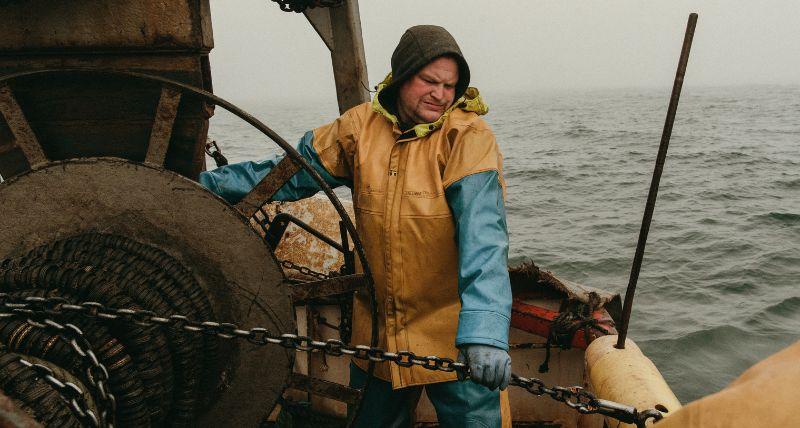 A fisherman at work on deck in full waterproofs hauling in the catch. Copyright Pete Robinson