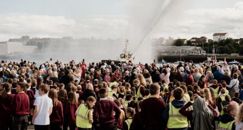 Crowds watch the Svitzer tug water jets at the unveiling of the Herring Girl sculpture in 2023